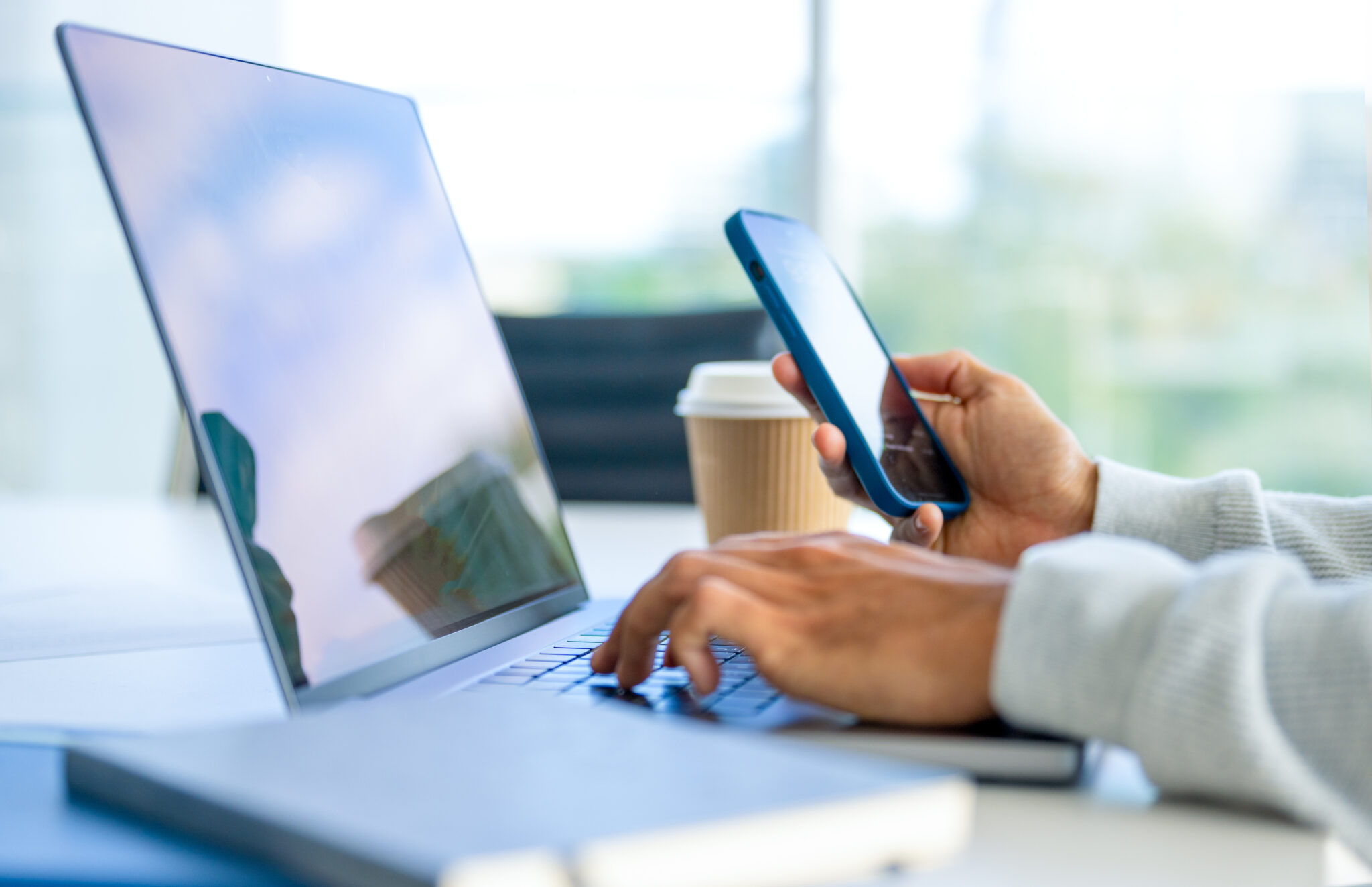 Close up of a Businessman working on a laptop computer and holding and looking at a mobile phone in the office.