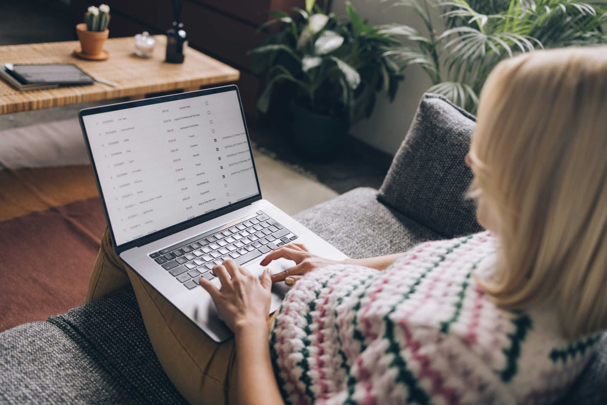 Unrecognizable Female Data Analyst Sitting Comfortably on a Grey Couch and Writing a Report on her Laptop