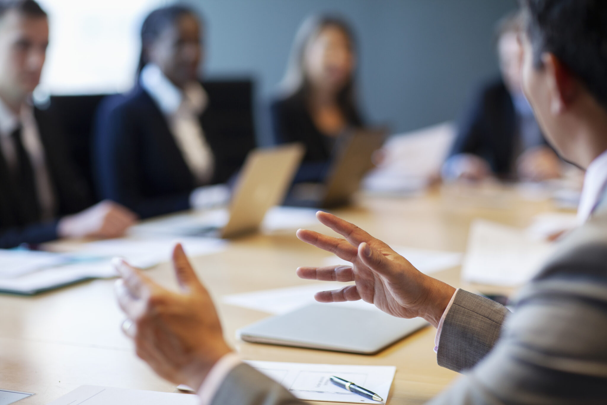 Hands of businessman gesturing ideas decisions in business meeting with group of work colleagues at board room conference table