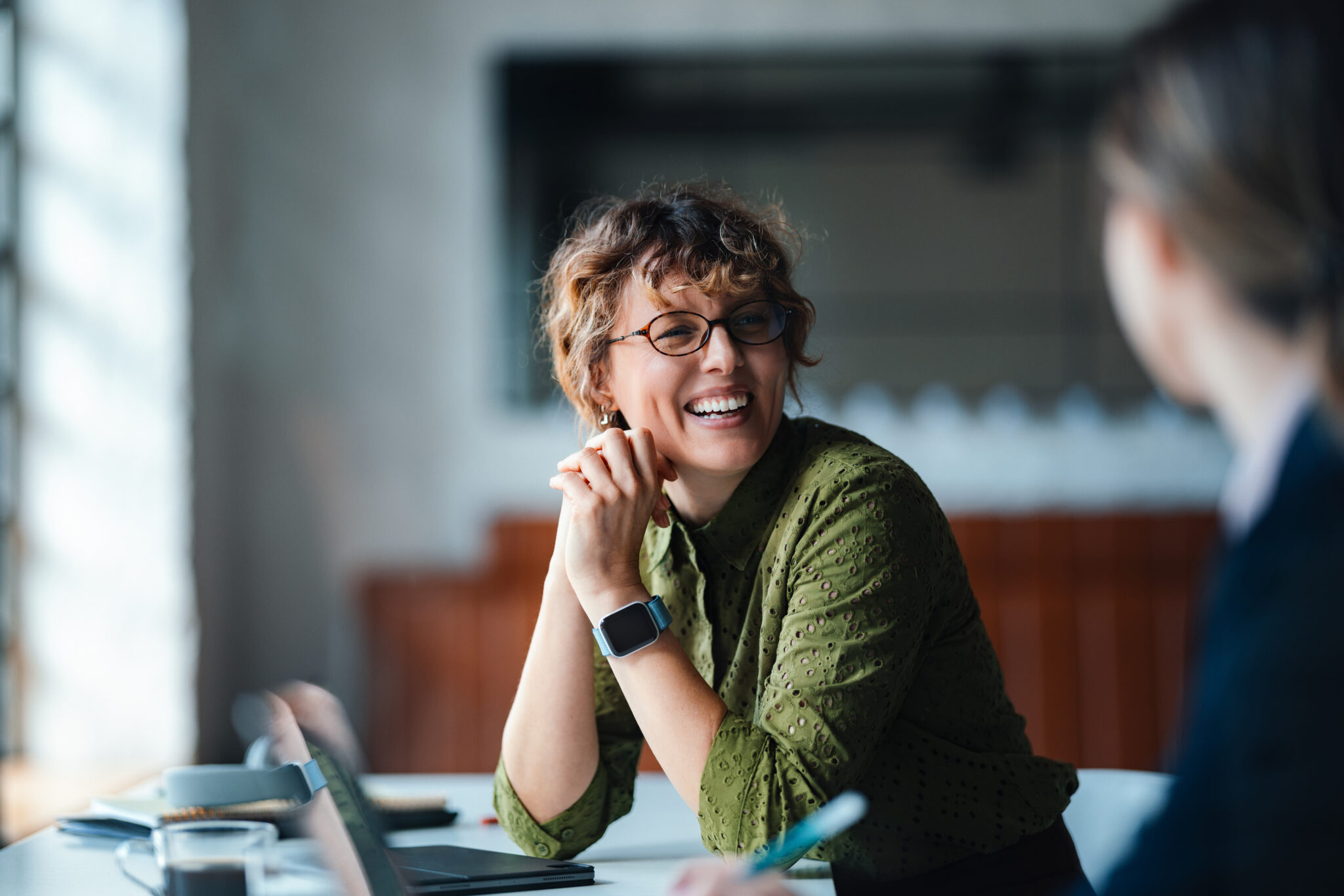 Smiling Woman in Green Shirt Engages in Casual Business Meeting at Modern Coworking Space